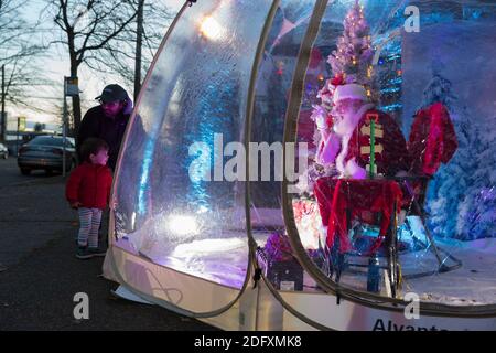 Seattle, Washington, Stati Uniti. 6 dicembre 2020. DaN Kemmis, noto come Seattle Santa, saluta una giovane famiglia da una bolla protettiva di plastica nel quartiere Greenwood di Seattle. Incapace di programmare eventi privati a causa della pandemia del coronavirus, Kemmis sta facendo apparizioni pubbliche fisicamente distanziate con alcune donazioni che avvantaggiano i rifugi locali dei senzatetto. Credit: Paul Christian Gordon/Alamy Live News Foto Stock