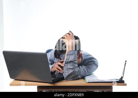 Un ritratto di un uomo asiatico con un'espressione stanca che lavora su report e libri informatici. Dipendente dell'ufficio con sfondo bianco isolato Foto Stock