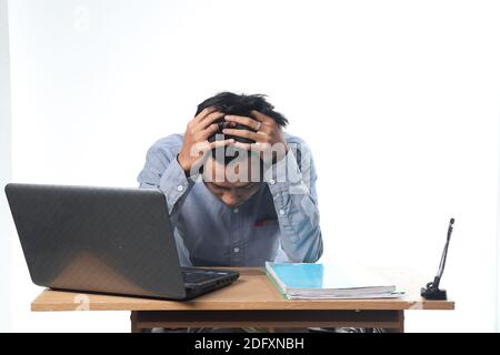 Un ritratto di un uomo asiatico con un'espressione stanca che lavora su report e libri informatici. Dipendente dell'ufficio con sfondo bianco isolato Foto Stock