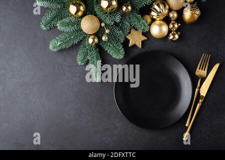 Tavolo di Natale o Capodanno con sfondo con piastra nera e posate di colore dorato. Vista dall'alto con spazio di copia per testo, elementi di disegno, grafica Foto Stock