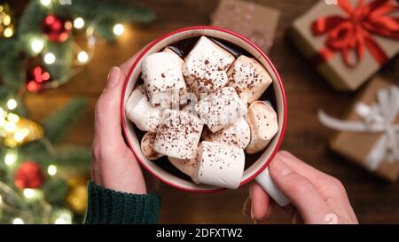 Cioccolata calda o bevanda di cacao con marshmallows in mani femminili. Cibo confortevole accogliente per le vacanze invernali Natale, Capodanno Foto Stock