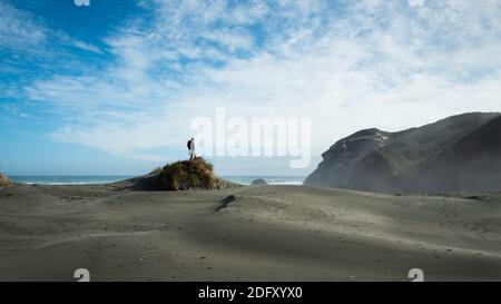 Uno zaino in spalla in piedi sulla cima della duna di sabbia su Wharariki Beach, South Island, Nuova Zelanda Foto Stock