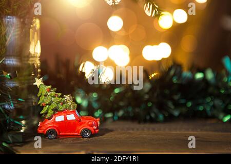 Decorazioni natalizie - l'auto rossa retrò porta l'albero di Natale con le scatole regalo sul tetto. Spazio per il testo. Anno nuovo. Giocattolo su ramo di abete con luci dorate Foto Stock