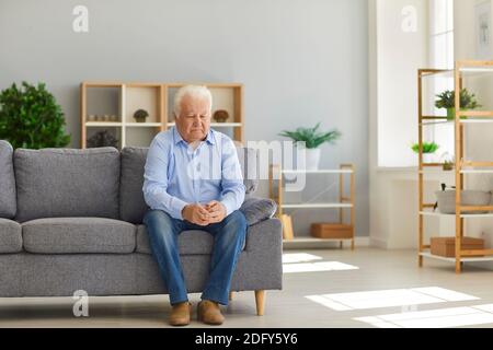 Uomo anziano seduto sul divano a casa sentendosi depresso, solitario e abbandonato dalla sua famiglia Foto Stock