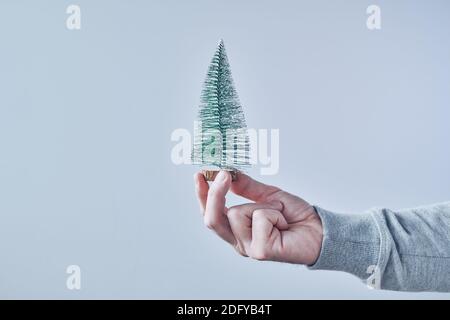 Mano che tiene il piccolo abete artificiale per la stagione di festa di Natale, spazio di copia incluso Foto Stock