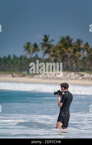 VARKALA, INDIA - Mar 14, 2020: Un foreigner con la sua macchina fotografica che cattura i Surfers nel mare Foto Stock