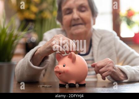 Donna anziana che mette una moneta in una banca piggy Foto Stock