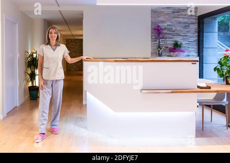 Ritratto di donna fisioterapista fiduciosa in piedi uniforme alla reception banco in ospedale o centro termale Foto Stock