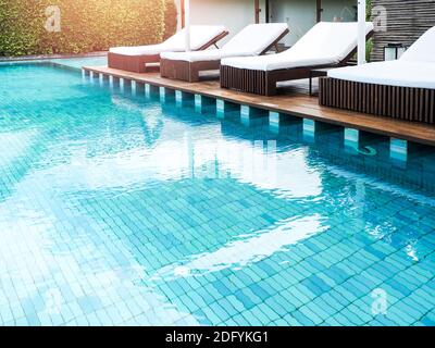 Lettini bianchi vuoti e puliti sulla terrazza in legno vicino alla piscina in estate. Foto Stock