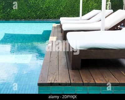 Lettini bianchi vuoti e puliti sulla terrazza in legno vicino alla piscina in estate. Foto Stock