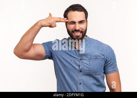 Uomo solitario depresso con barba che tiene le dita vicino al tempio fingendo di tenere la pistola, andando a fare colpo, di fronte a problemi e crisi. Monolocale interno Foto Stock