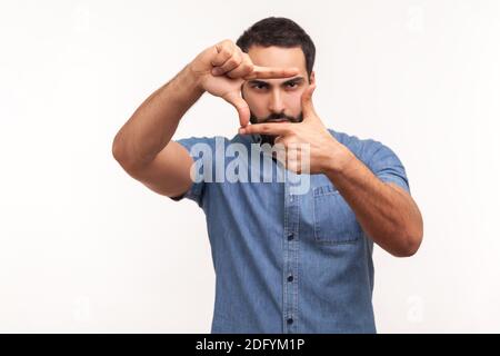 Concentrato uomo bearded paparazzi in cerca di messa a fuoco correttamente per fare scattare foto, tenendo le dita come cornice, visione cameraman. Studio interno girato è Foto Stock