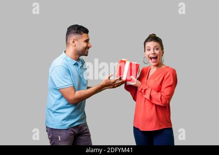 Il modo migliore per presentare per la donna. Giovane uomo in abiti casual dando confezione regalo per piacevolmente sorpreso donna che guarda la fotocamera con bocca aperta, bonus inaspettato. Foto Stock