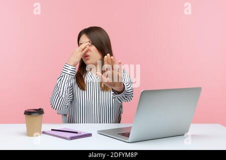 Confuso donna dipendente ufficio seduto sul posto di lavoro con il computer portatile e trattenendo il respiro, pizzicando il naso per evitare un terribile pupore, gesturing stop. Stu. Interno Foto Stock