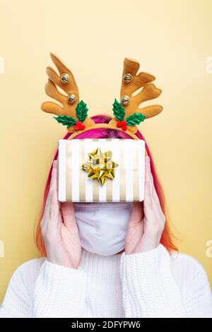 Ragazza in pullover bianco, cervo e indossare maschera protettiva sul viso, contiene regalo copertura viso, sfondo giallo Foto Stock