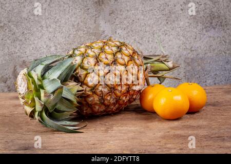 Ananas e arance su vecchio tavolo di legno d'annata Foto Stock