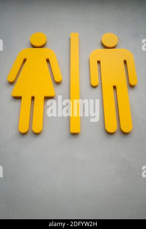 Simboli gialli fianco a fianco della donna e dell'uomo del pubblico insegna della toilette su una parete di cemento Foto Stock