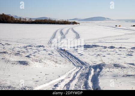 Traccia da motoslitta su un lago innevato con pescatori in lo sfondo Foto Stock