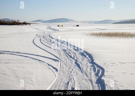 Traccia da auto su un lago nevoso con pescatori in lo sfondo Foto Stock