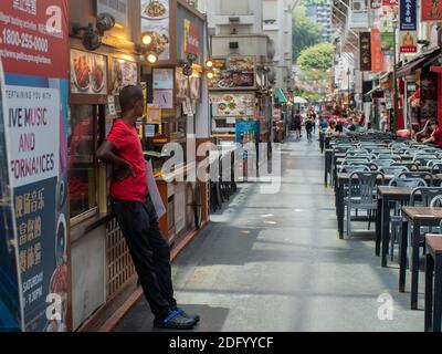 Un uomo guarda su tavoli vuoti in un campo alimentare falchiere nel centro di Singapore, se Asia. Foto Stock