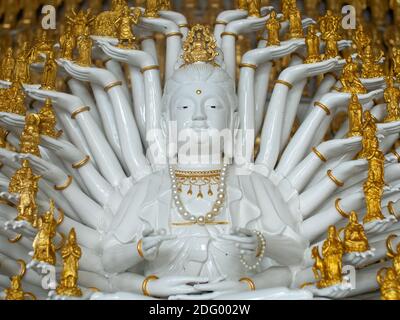 Una statua bianca e dorata di Buddha con molte braccia in un tempio a Hat Yai, Thailandia. Foto Stock