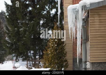 Costruzione del tetto coperta di icicles taglienti, appeso ad un tubo di scarico Foto Stock