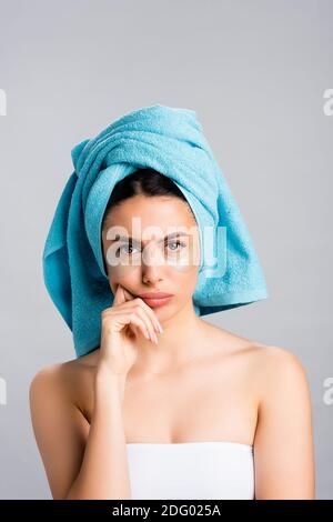 triste bella donna con asciugamano blu su capelli e idrogel macchie oculari sulla faccia isolate su grigio Foto Stock