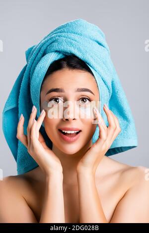 stupito bella donna con asciugamano blu su capelli e idrogel macchie oculari sulla faccia isolate su grigio Foto Stock