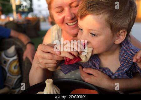 Nonna che alimenta il nipote khinkali in ristorante Foto Stock