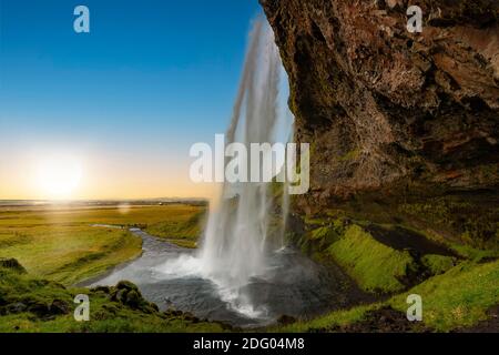 Vista attraverso la cascata Seljalandsfoss in Islanda al tramonto Foto Stock