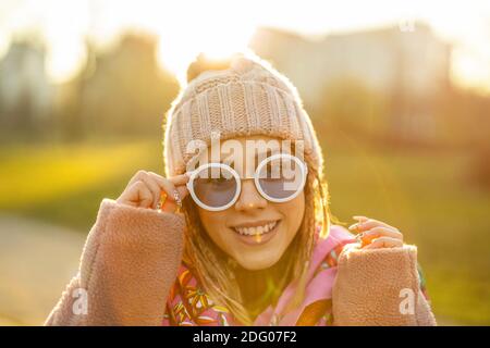 Ritratto di giovane donna che indossa cappello a maglia, sciarpa colorata e occhiali da sole durante l'inverno Foto Stock