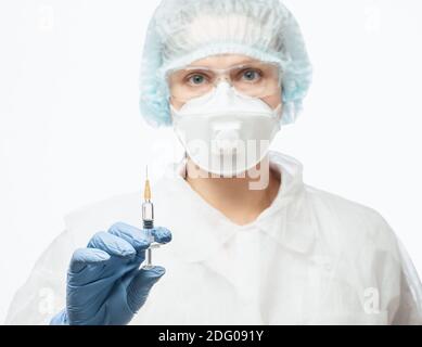 Primo piano di un medico che indossa tuta protettiva PPE, occhiali e maschera facciale FFP3 contenente siringa pronta per l'iniezione di un vaccino o di un medicinale Foto Stock