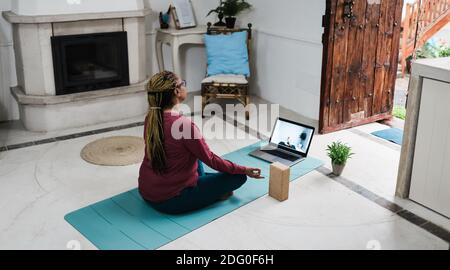 Donna anziana africana che fa la lezione di yoga in linea a casa durante Epidemia di coronavirus - Vecchia persona femminile meditante utilizzando un computer portatile - tecnologia AN Foto Stock