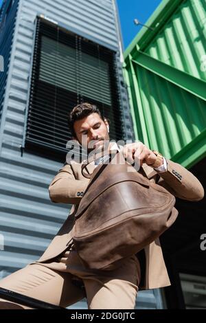 vista ad angolo basso di un uomo d'affari con braccio in possesso di auricolari wireless borsa in pelle Foto Stock