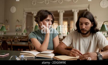 Giovani studenti attraenti che fanno i compiti insieme nella biblioteca del college. Studenti che studiano all'università Foto Stock