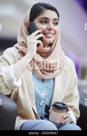 Ritratto verticale di bella donna medio-orientale che indossa foulard mentre si parla con smartphone nel centro commerciale Foto Stock
