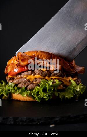 Un colpo verticale di un hamburger grande e un cleiver coltello su sfondo nero Foto Stock
