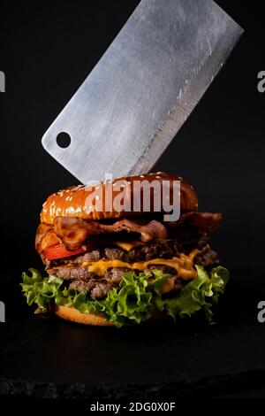 Un colpo verticale di un hamburger grande e un cleiver coltello su sfondo nero Foto Stock