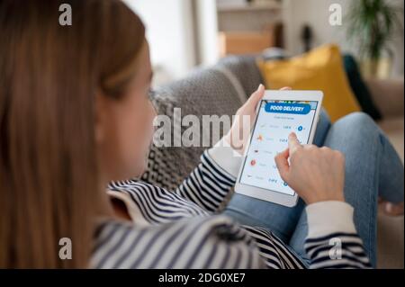 Giovane donna con tablet che ordina cibo a casa, coronavirus e concetto di consegna di cibo. Foto Stock