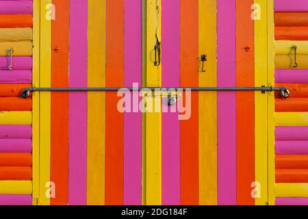 primo piano della parte anteriore di una capanna di legno dipinta a strisce arancioni, gialle e viola. Foto Stock
