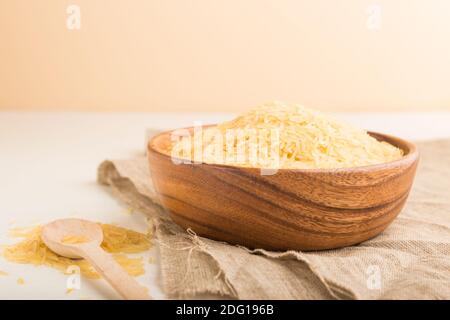 Ciotola in legno con riso dorato crudo e cucchiaio di legno su fondo di legno bianco e tessuto di lino. Vista laterale, primo piano, messa a fuoco selettiva. Foto Stock