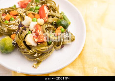 Tagliatelle di spinaci verdi con pomodoro, piselli e germogli di microsverde su fondo di legno bianco e tessuto giallo. Vista laterale, primo piano, selezione Foto Stock