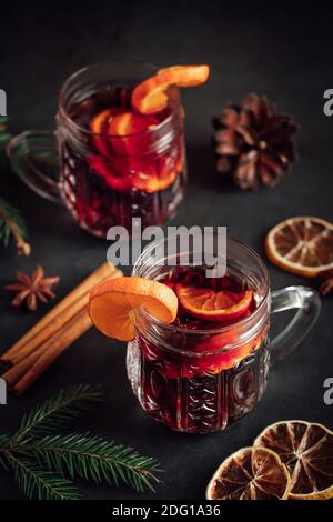 Due bicchieri di VIN brulé caldo con frutta e spezie su sfondo scuro. Inverno caldo vacanza drink. Foto Stock