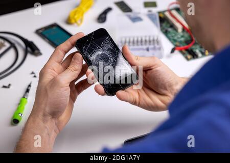 smartphone con schermo rotto incrinato nelle mani del tecnico. servizio di riparazione del telefono Foto Stock