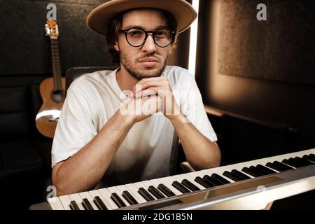 Giovane bel produttore di musica che guarda con sicurezza in macchina fotografica su cui lavora nuovo album musicale nel moderno studio di registrazione Foto Stock