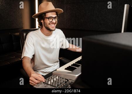 Giovane musicista allegro ed elegante che lavora felicemente al nuovo album in studio di registrazione moderno Foto Stock