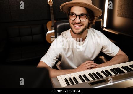 Giovane musicista elegante e attraente che lavora felicemente in un moderno studio di registrazione. Uomo sorridente che compone la canzone in studio Foto Stock