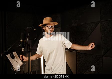 Un musicista elegante e attraente che danzano mentre registra una nuova canzone in uno studio moderno. Giovane cantante maschile che canta in studio Foto Stock