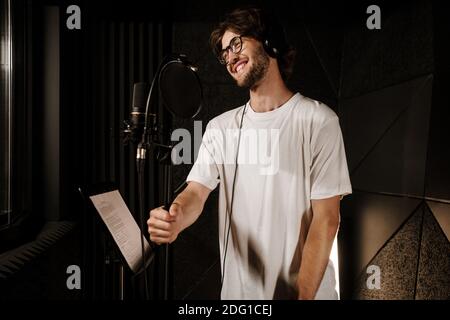 Attraente cantante sorridente in cuffie felicemente registrare canzone in professionale studio audio Foto Stock