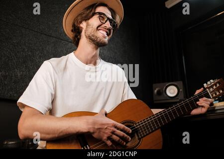 Elegante uomo che canta e suona con una chitarra in studio. Giovane musicista che registra una nuova canzone in studio moderno Foto Stock